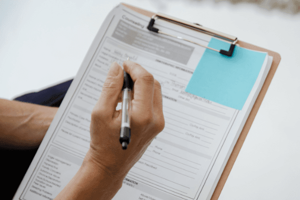 Image of a hand and pen filling out a survey on a clipboard.